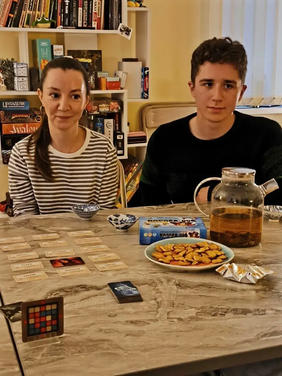 Игроки за столом с разложенной настольной игрой, чаем и печеньем